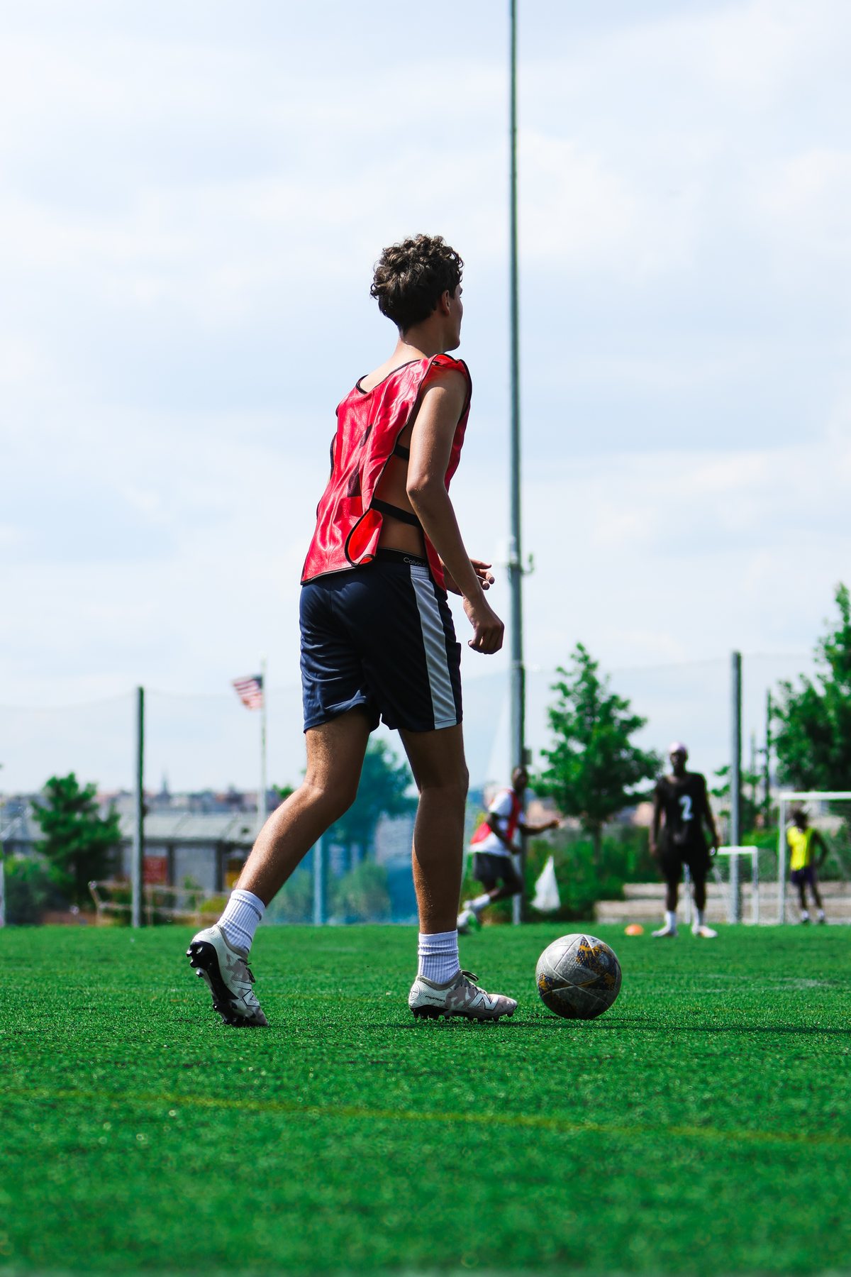 A player in a red bib walking with the ball on the pitch